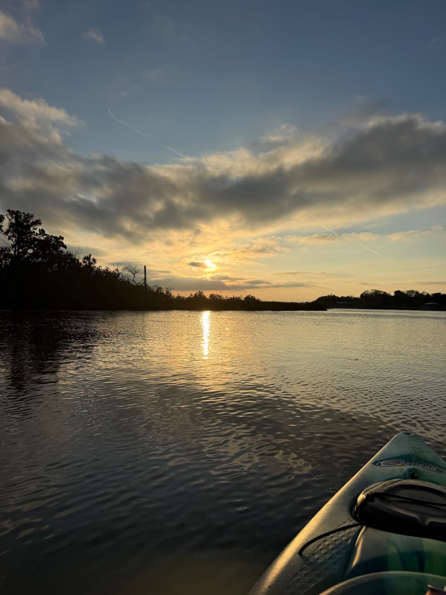 From the bow of a kayak on Mason Creek at sunset — glassy water, the sun low over the mangrove treeline at The Rusty Hook Riverhouse, Old Homosassa, Florida