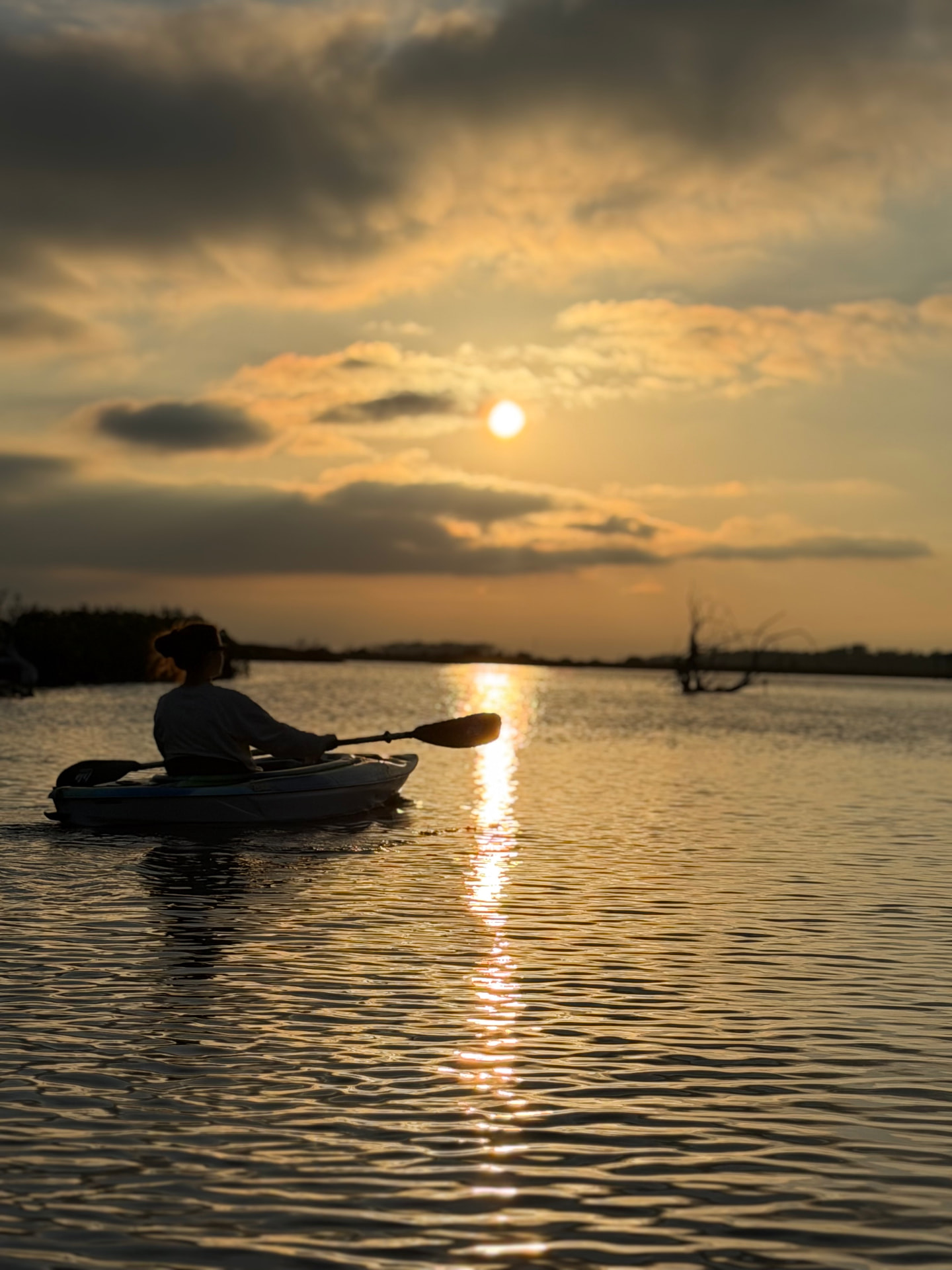 A kayaker on Mason Creek silhouetted against the sun going down, the light running back across the water at The Rusty Hook Riverhouse, Old Homosassa, Florida