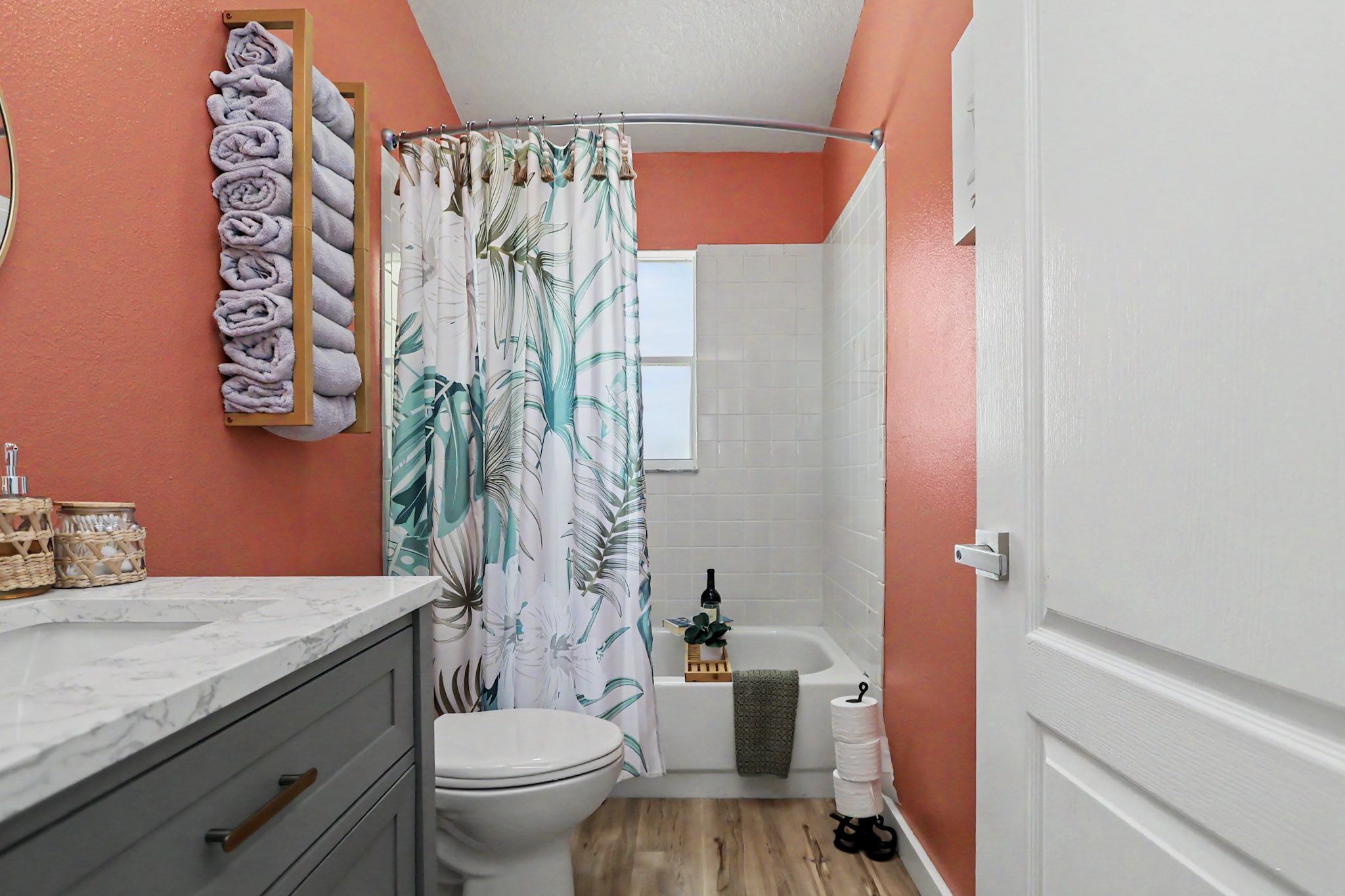 Coral-walled bathroom with rolled towels, palm-print curtain and a marble-topped vanity