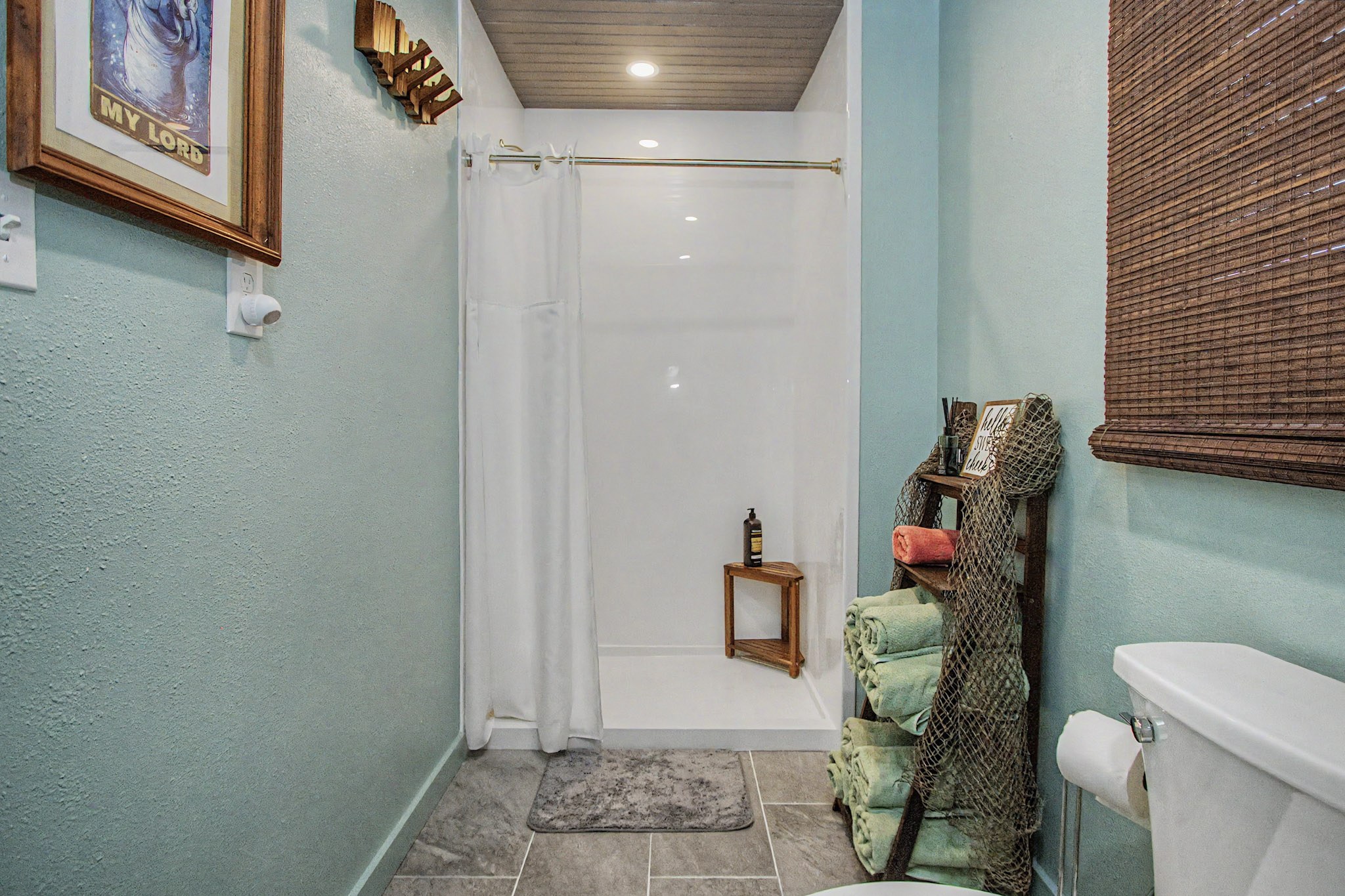 The third, downstairs bathroom — soft aqua walls, a white walk-in shower, tiled floor and rolled towels on a net-wrapped ladder rack