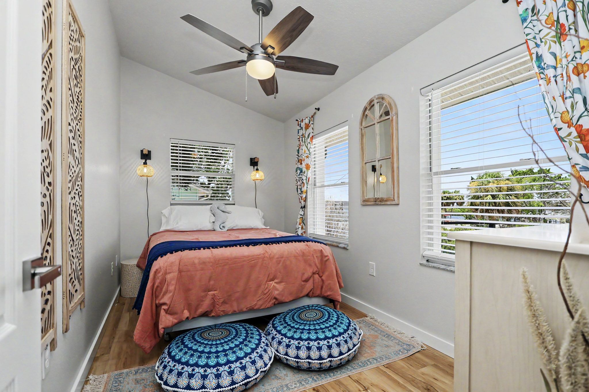 Guest bedroom with a coral bedspread, patterned aqua floor cushions and carved wood screens