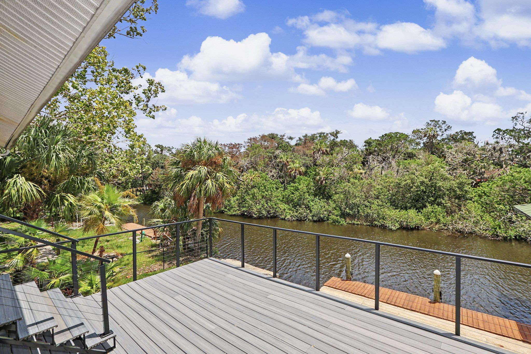 Open waterfront deck with cable railings and loungers looking straight down the waterway