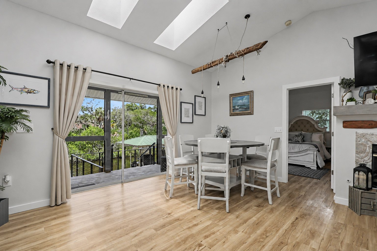 The dining room under skylights and a driftwood pendant, with the sliders open onto the porch and the water beyond