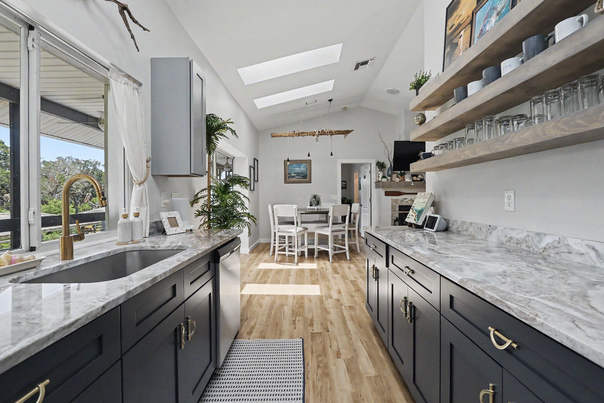Long galley kitchen with navy cabinetry, veined stone counters, brass hardware and open timber shelving