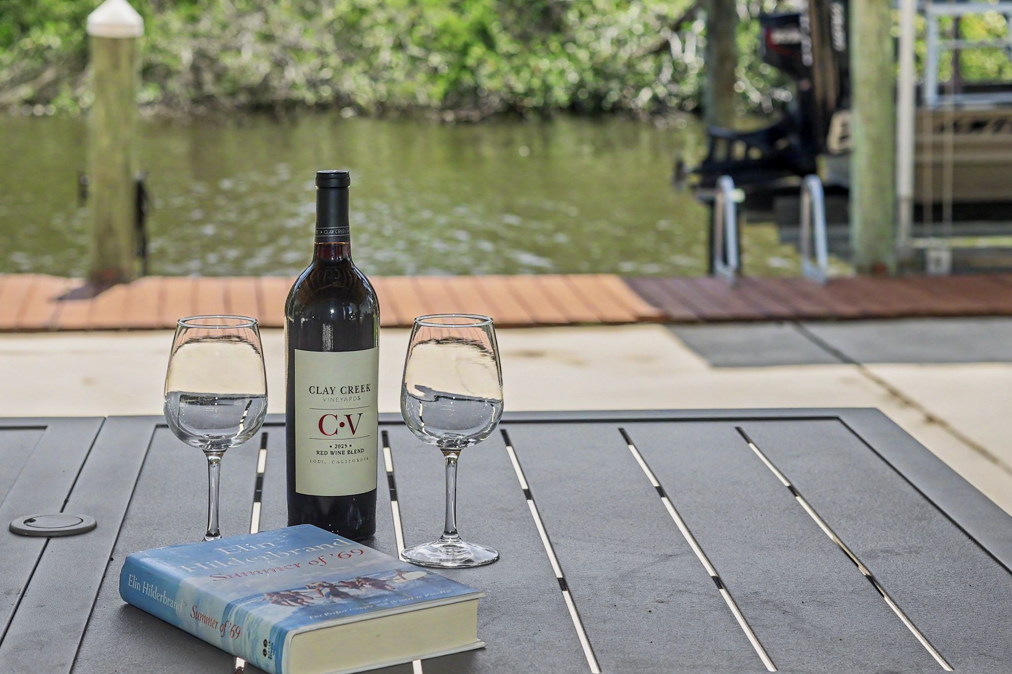 A bottle of wine and two glasses resting on the dock rail with the water and mangroves behind